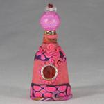 Small pink Genie bottle embellished with a beaded lid. The genie inside watches over a dangling key. Perhaps the key to your greatest wish? 